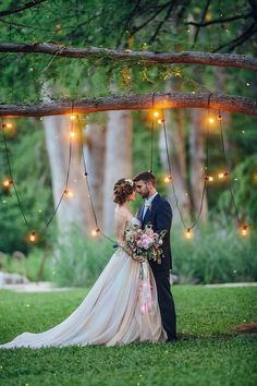 a bride and groom standing under a tree with fairy lights hanging from it's branches