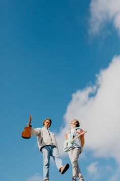 two people standing on top of a hill with guitars in their hands and one holding a guitar