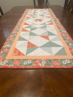 a table runner with an orange and green design on it sitting on top of a wooden table