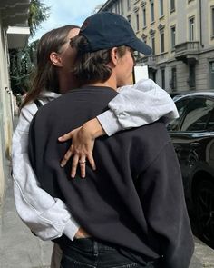 a man and woman kissing on the street in front of a building with cars behind them