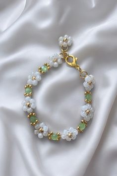 a white bracelet with green beads and gold accents on a white silk background, close up