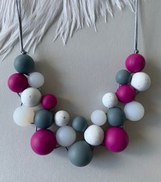 a necklace made out of different colored beads on a white surface with feathers in the background