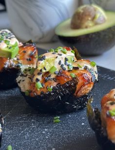 some sushi is on a black plate with avocado and other food items