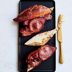 three pieces of bacon sitting on top of a black plate next to a butter knife