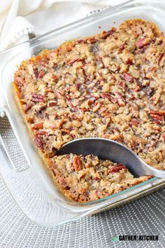 a glass casserole dish with a spoon in it and pecans on the side