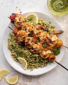 a white plate topped with shrimp, rice and lemon wedges next to a glass of green pesto