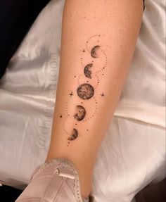 a woman's arm with phases of the moon and stars tattooed on her leg