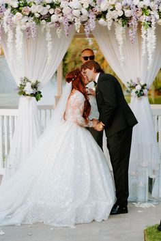 a bride and groom kissing in front of an outdoor wedding ceremony arch with white flowers