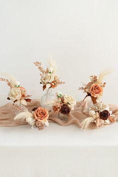 three vases filled with flowers and feathers on top of a white cloth covered table