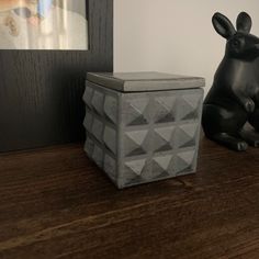 a black rabbit statue sitting next to a gray box on top of a wooden table