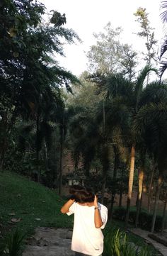 a person standing in front of some trees with their hands on their head and looking at the ground