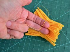 a hand holding a yellow piece of cloth on top of a green surface with thread