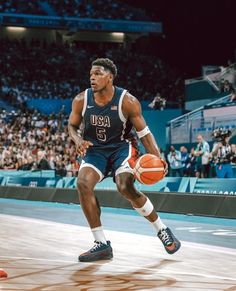 a basketball player dribbles the ball during a game in front of an audience