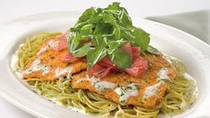 a white plate topped with pasta covered in sauce and garnished with green leaves