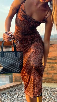 a woman in a leopard print dress carrying a black handbag