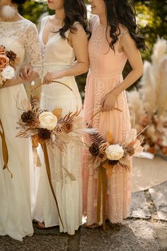 three beautiful women standing next to each other in dresses and holding bouquets with feathers on them