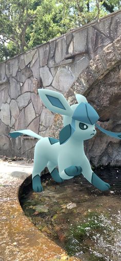 a statue of a blue and white pokemon sitting on top of a rock wall next to a river