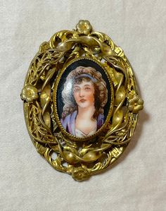 This antique brooch is a stunning piece of jewelry that will surely catch anyone's attention. Made of ornate gold gilded brass and adorned with an intricate hand-painted porcelain medallion, this brooch is a true masterpiece. It features a painted portrait of a lovely middle aged lady and signed underneath.. The brooch is perfect for collectors of antique jewelry and those who appreciate the beauty of unique pieces. Its intricate design and attention to detail make it a true conversation starter Ornate Gold Collectible Brooches, Ornate Medallion Brooches For Collectors, Ornate Medallion Brooches For Collectibles, Ornate Antique Gold Brooches For Collectors, Antique Gold Enamel Brooches, Victorian Gold Enamel Pin, Victorian Style Gold Enamel Pin, Antique Enamel Cabochon Brooches, Victorian Enamel Collectible Pin