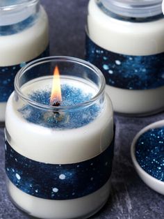 three candles with blue and white designs on them sitting next to each other in glass jars