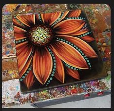 an orange flower painted on top of a piece of art