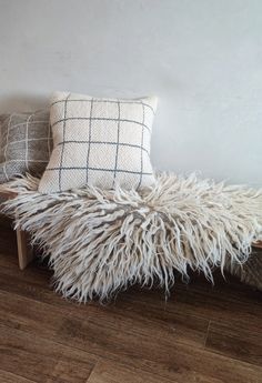 two pillows sitting on top of a wooden bench next to a white wall and wood floor