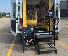 the back end of an open van with bookshelves on it and a sign in front