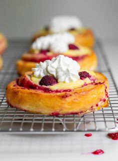 small pastries with whipped cream and raspberry toppings on a cooling rack