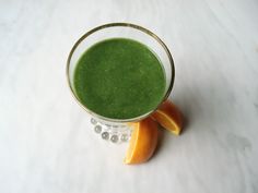 a green smoothie in a glass with an orange slice on the rim and garnish