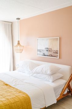 a bed with white linens and pillows in a pink room next to a window