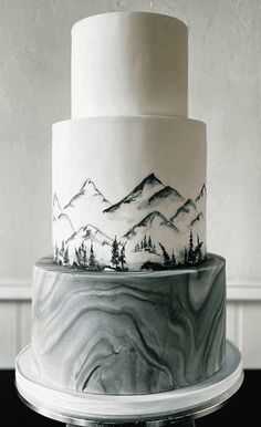 a three tiered white and black cake with trees on it