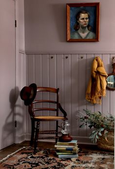 a room with a chair, rug and painting on the wall next to a potted plant