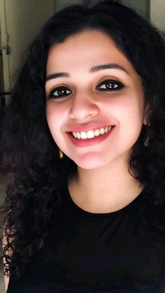 a woman with curly hair smiling at the camera and wearing a black shirt, gold hoop earrings