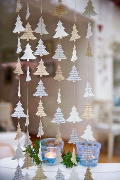 paper christmas trees hanging from the ceiling with candles in front of them on a table