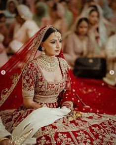 a woman in a red and gold bridal gown sitting on the floor with people behind her