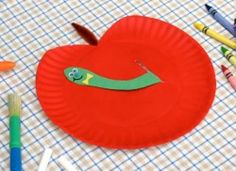 a paper plate with a worm on it next to crayons and pencils