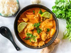 a bowl filled with curry and meat next to some vegetables on a table top,