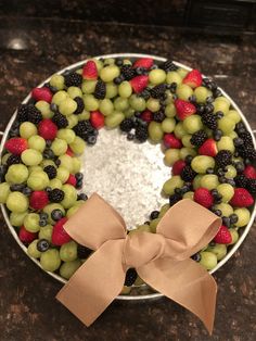 a cake decorated with grapes, raspberries and blackberries on a plate next to a bow