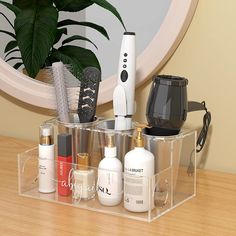 an assortment of personal care products in a clear container on a wooden table next to a potted plant