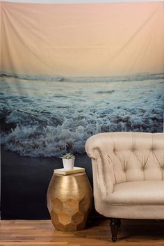 a chair and vase sitting in front of a wall with a tapestry hanging on it