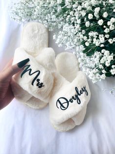 two personalized slippers sitting on top of a bed next to a bouquet of flowers