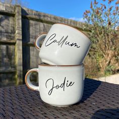 two coffee mugs sitting on top of a table next to each other with writing on them