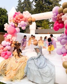 a group of children dressed in princess dresses are gathered around an arch made out of balloons