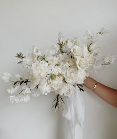 a bouquet of white flowers is being held by a woman's hand in front of a wall