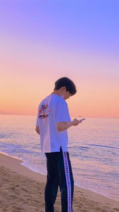 a man standing on top of a sandy beach next to the ocean holding a cell phone