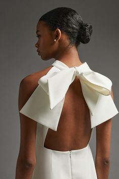 the back of a woman wearing a white dress with a large bow on her neck