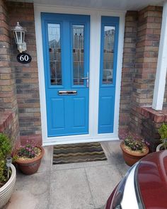 a blue front door with two potted plants next to it and a red car parked in front