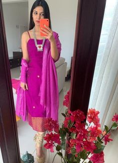 a woman taking a selfie in front of a mirror wearing a purple dress and pink scarf