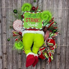 Add a playful twist to your holiday decor with this green monster wreath! Featuring the iconic green legs and the fun "Stink! Stank! Stunk!" sign, this wreath is perfect for anyone who loves a bit of holiday humor. Decked out with bright, festive ribbons, ornaments, and whimsical details, this unique wreath will make a statement on any door or wall. Grinch Wreath Ornaments, Red And Green Christmas Wreath, Grinch Wreath For Sale, Green Monster Wreath, Elf Christmas Wreath, Green Christmas Wreath, Traditional Christmas Wreath, Stink Stank Stunk, Monster Wreath