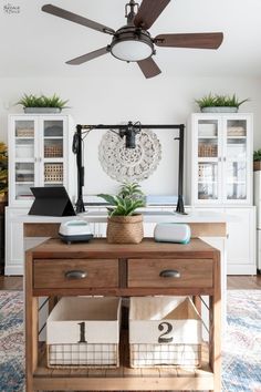 a living room area with a table, fan and baskets on the counter top in front of it