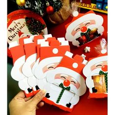 a person holding up some christmas cards with santa clause on them and presents in the background